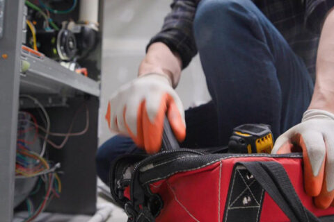 A person in gloves kneels by an open electrical panel