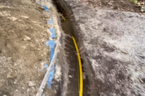 A narrow trench with a yellow pipe buried under soil