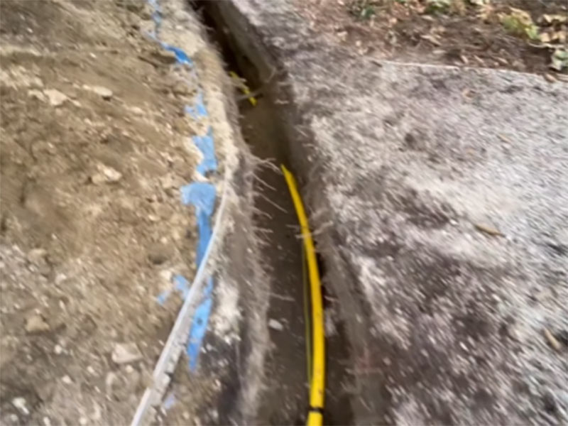 A narrow trench with a yellow pipe buried under soil A narrow trench with a yellow pipe buried under soil
