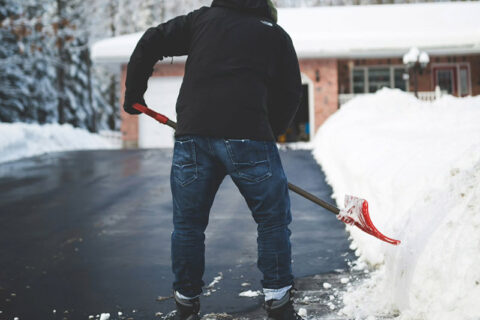 A man wearing a winter coat and hat shoveling heavy snow off a residential driveway